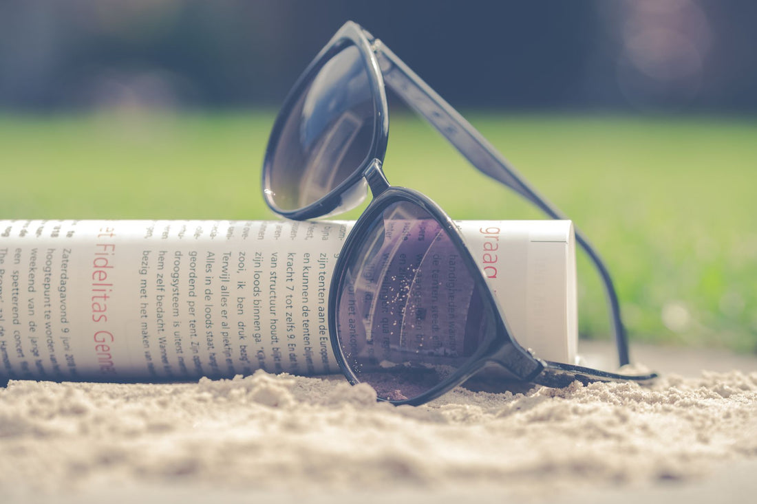 Chic black sunglasses resting with a rolled newspaper in the sand on a sunny summer day.
