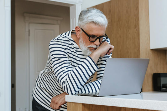 A senior adult man with glasses concentrating on his laptop at home, symbolizing modern working environments.