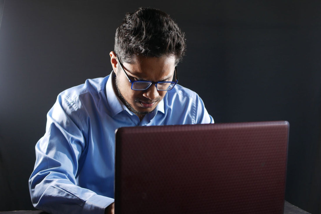 Serious man in dress shirt working on a laptop against a gray background.