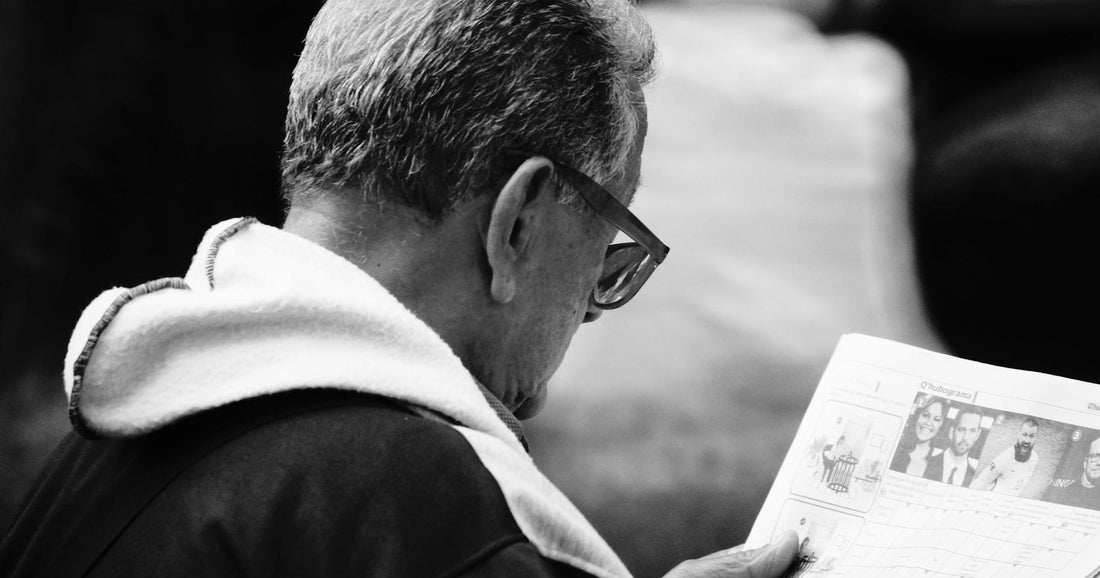 Elderly man in glasses reading a newspaper, depicted in a black and white portrait.