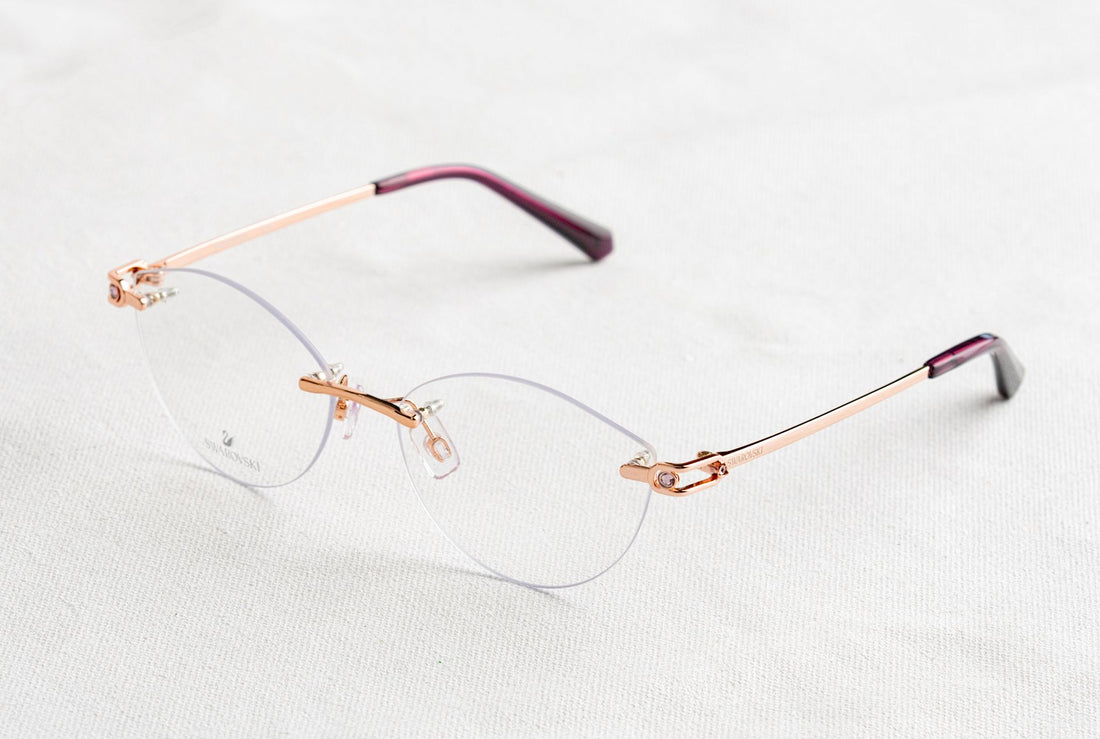Close-up of stylish rimless eyeglasses with golden temples on a white background.