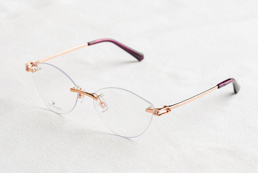 Close-up of stylish rimless eyeglasses with golden temples on a white background.