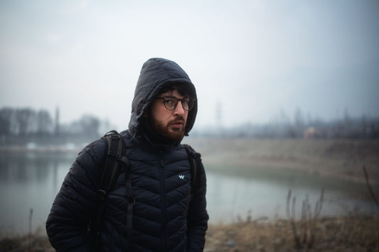 Man wearing glasses and winter jacket standing by a foggy lake, exuding a contemplative mood.