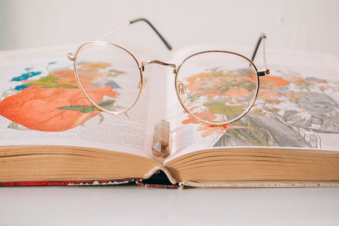 A pair of eyeglasses resting on an open book filled with colorful illustrations and drawings.