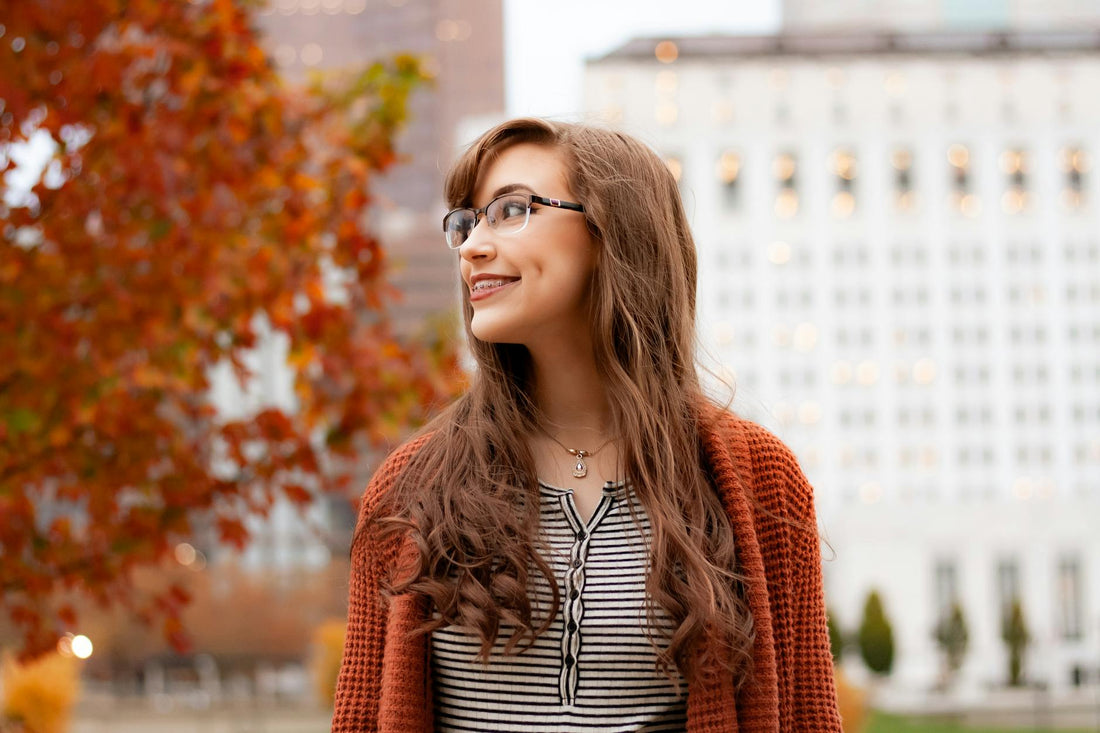 Portrait of a young woman with glasses smiling outdoors in a city during autumn.