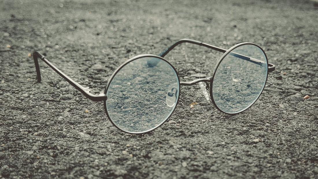 Classic round eyeglasses with a vintage design resting on textured asphalt. Ideal for retro themes.