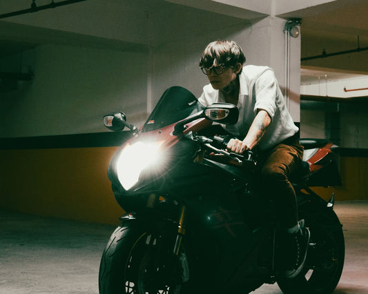 A man on a motorcycle in a dimly lit parking garage with headlight on, creating a dramatic atmosphere.