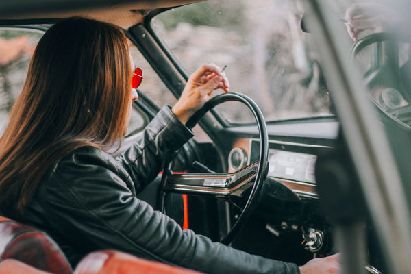 A stylish woman smoking inside a vintage car, showcasing a relaxed and nostalgic atmosphere.