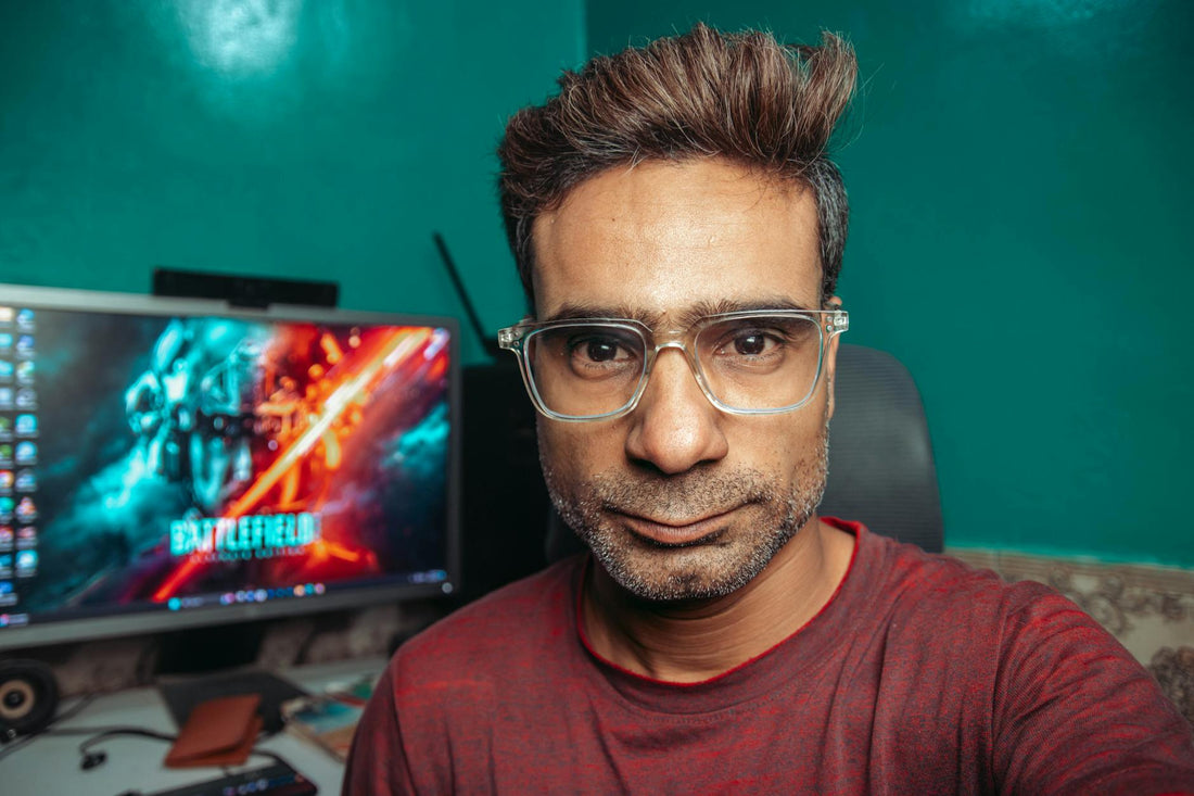 A man with glasses poses for a selfie in his home office, with a computer screen in the background.