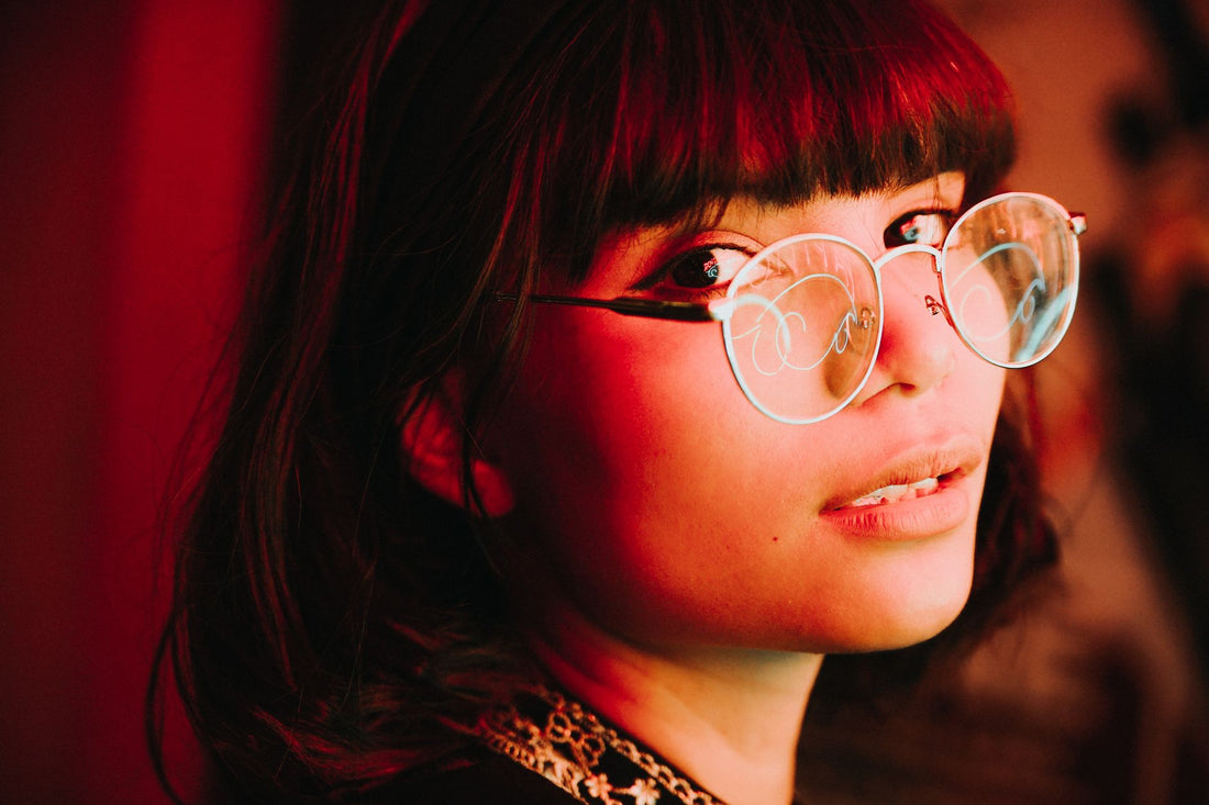 Young woman with eyeglasses, posing under red ambient lighting.