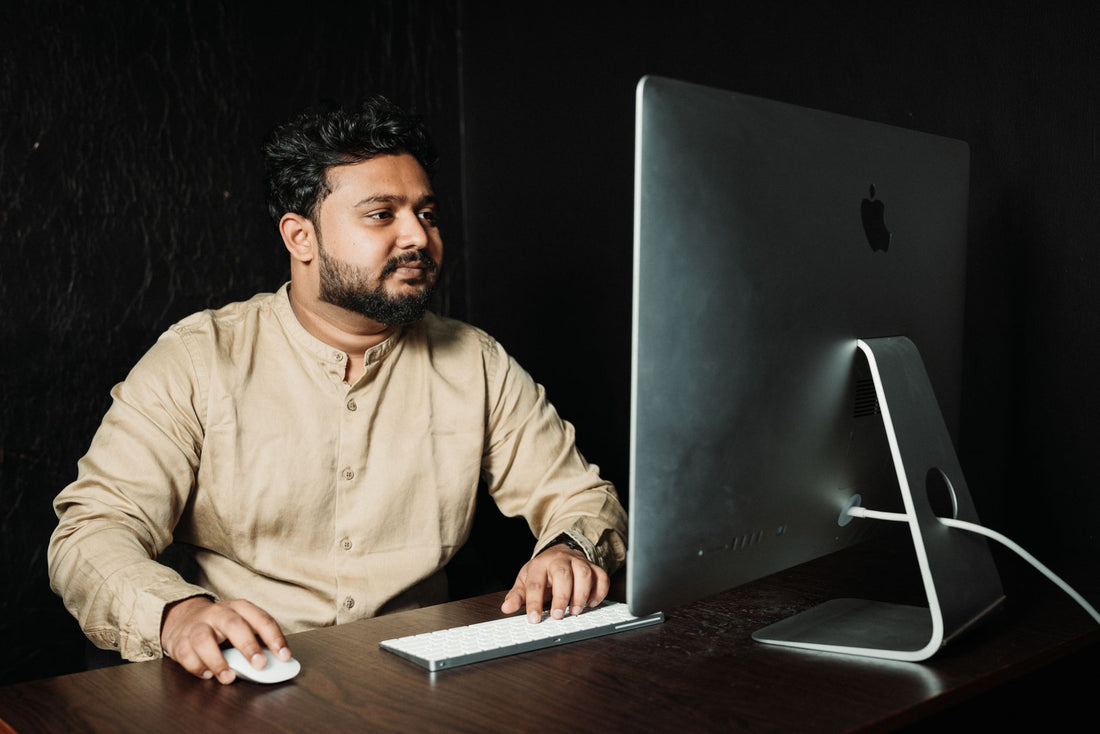 Man in formal attire working at a computer in a dimly lit office setting.