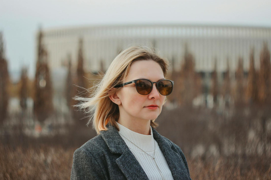 Portrait of a woman in sunglasses and gray jacket, set against an outdoor background.