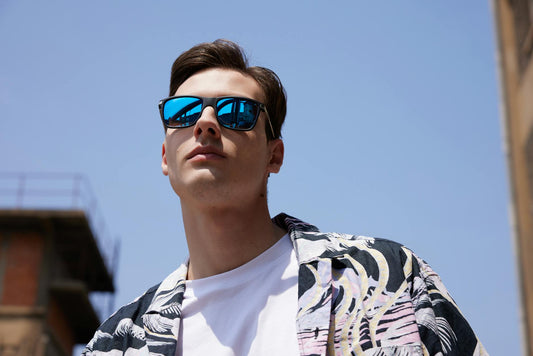 A fashionable young man wearing reflective sunglasses and a casual summer outfit outdoors.