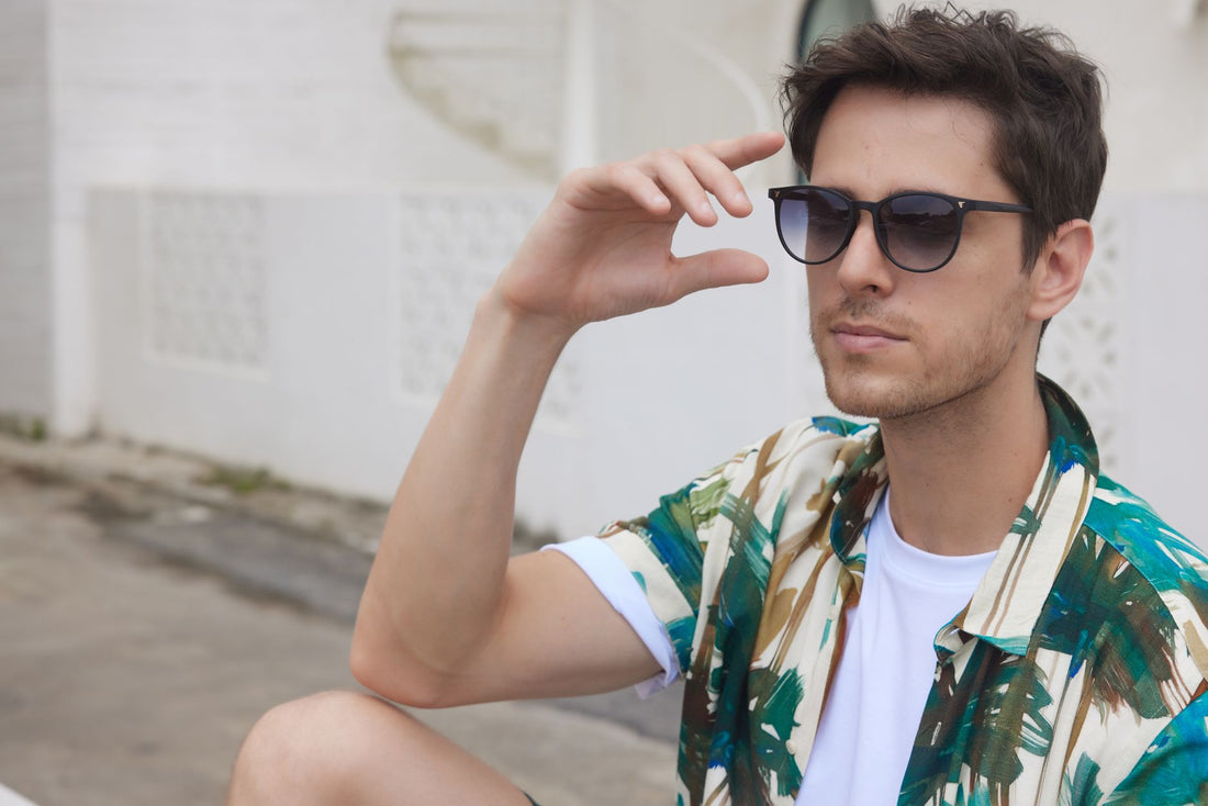 Trendy man wearing sunglasses and a colorful shirt, enjoying a sunny day outside.