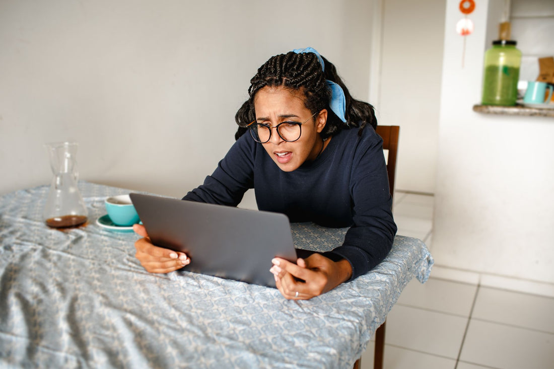 A woman with glasses intently focusing on her laptop screen at a dining table indoors.
