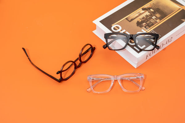 Stylish eyeglasses and books on an orange backdrop showcase modern design and fashion.