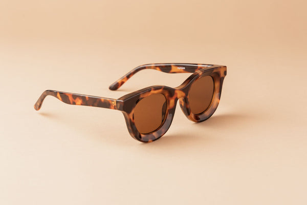 Elegant tortoiseshell sunglasses with brown lenses creatively displayed on a simple beige backdrop.