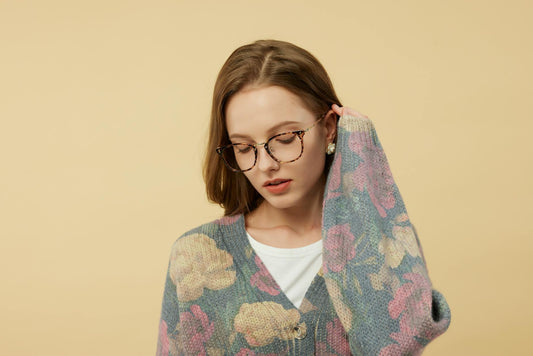 Portrait of a woman wearing stylish eyeglasses and a floral sweater in a photo studio.