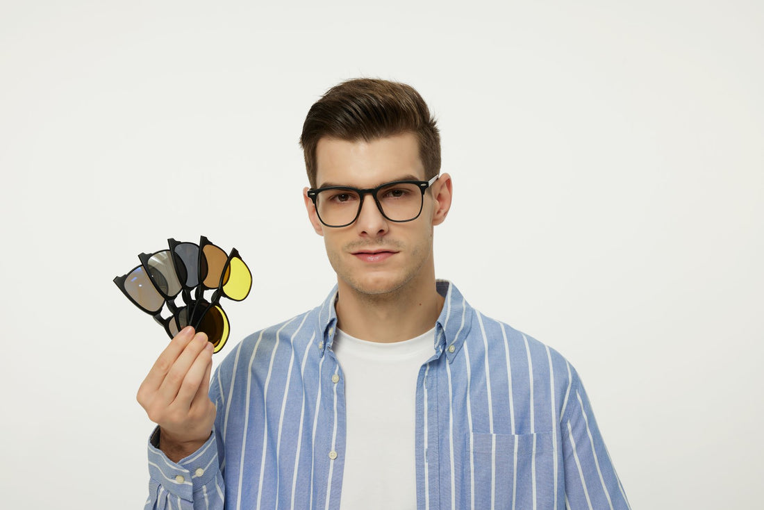 Fashionable young man with glasses holding a set of interchangeable lenses for a stylish look.