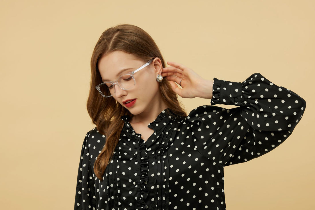 Stylish woman with glasses in polka dot blouse against a beige backdrop.