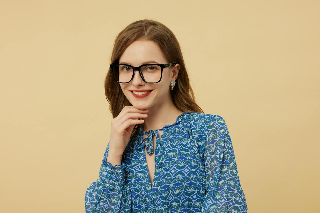 Portrait of a stylish woman wearing glasses and a blue patterned blouse against a beige background.