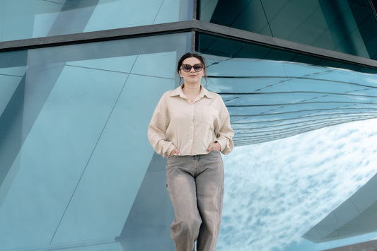 Confident woman in casual attire posing in front of modern geometric glass architecture.