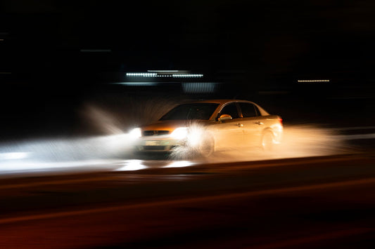 A car speeding through a wet road with dramatic splashes during a nighttime drive.