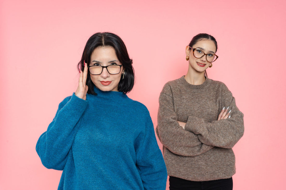 Two confident women posing stylishly in glasses, against a pink backdrop.