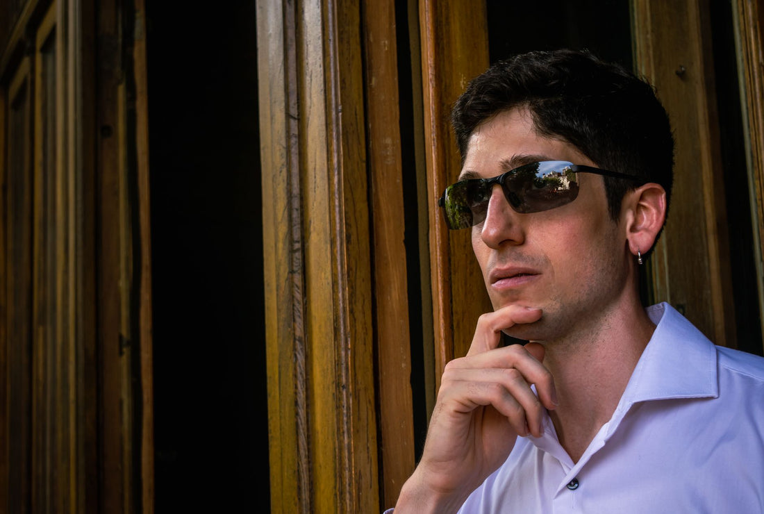 A thoughtful man wearing sunglasses stands by wooden panels, deep in contemplation.