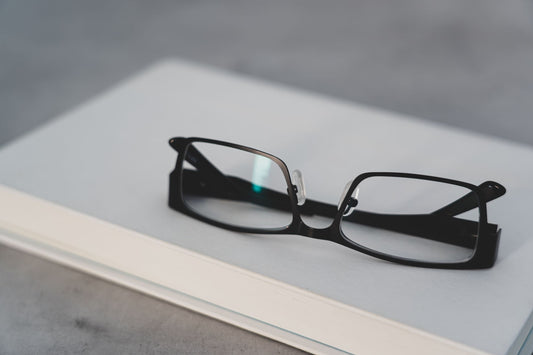 A pair of stylish black reading glasses rests on a closed book for a modern touch.