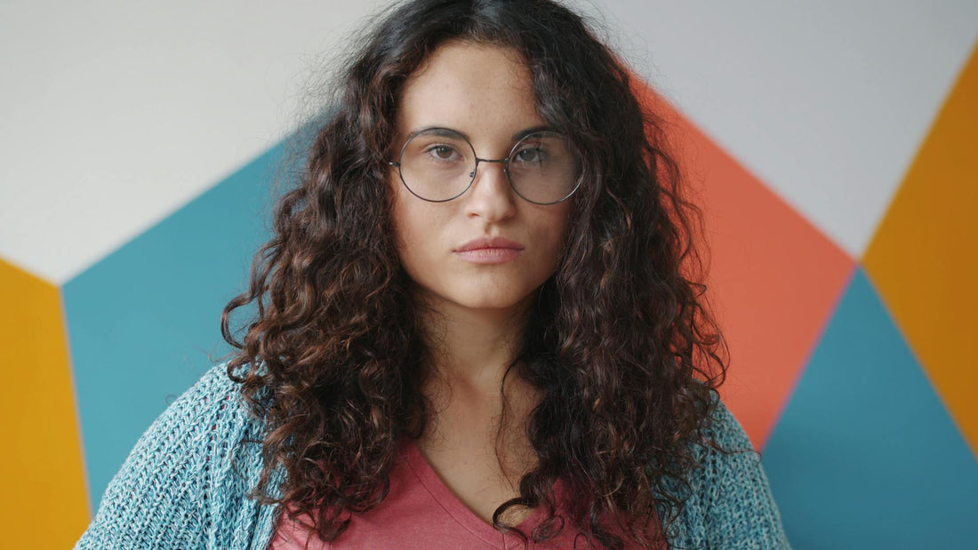 Portrait of a woman with curly hair and glasses against a colorful geometric background.