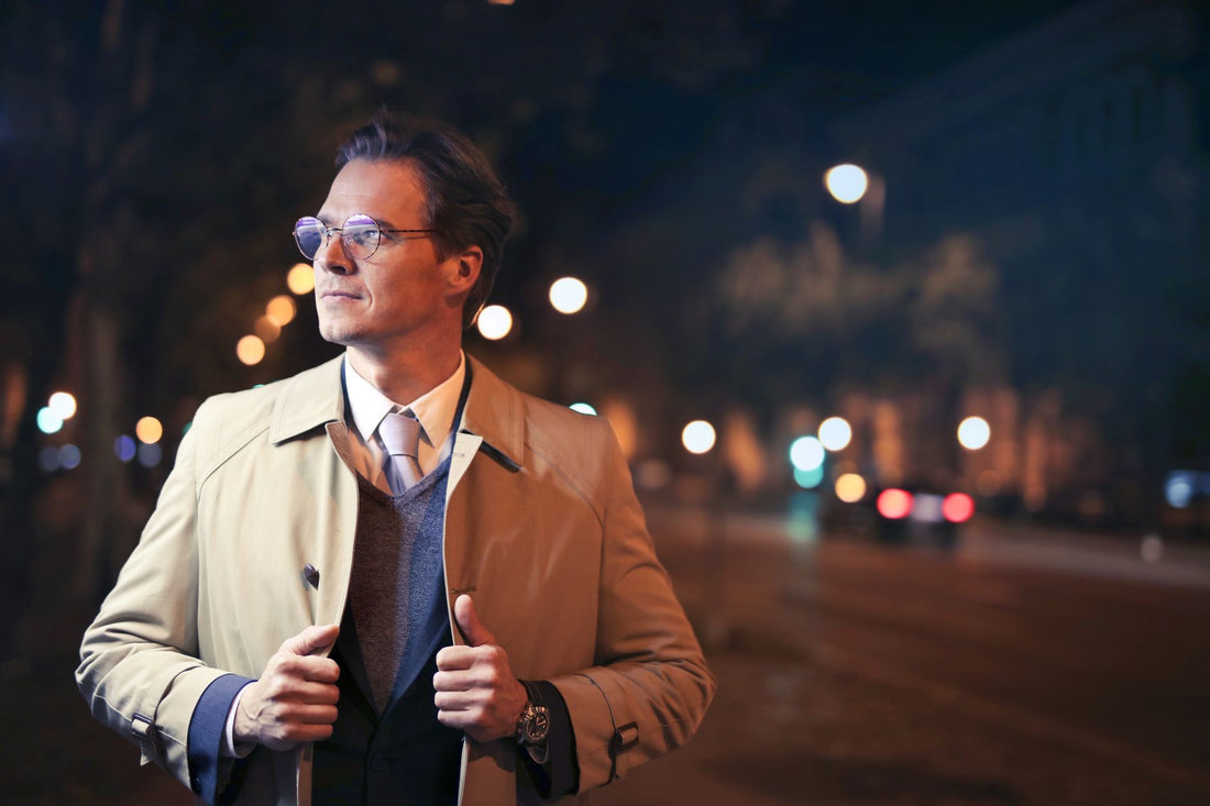Elegant man in a trench coat walking city streets at night with bokeh lights.