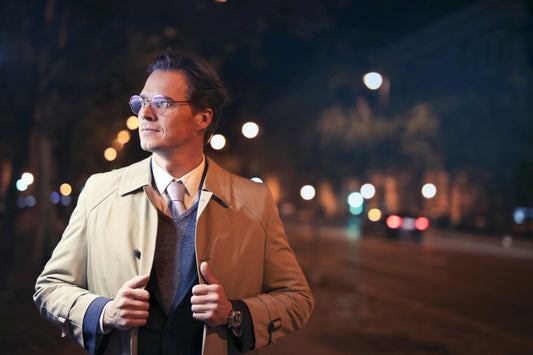 Elegant man in a trench coat walking city streets at night with bokeh lights.