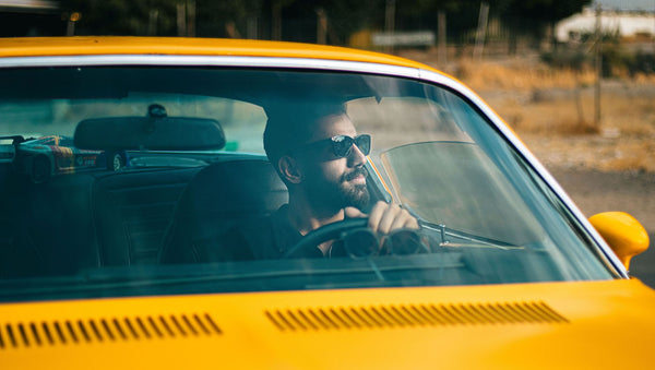 A bearded man enjoys driving a classic yellow car on a sunny day.