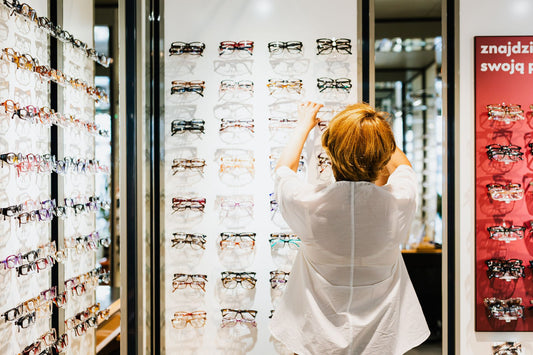 A woman browsing eyeglasses on a display shelf in an optical store.