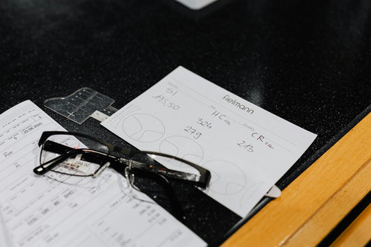 Eyeglasses resting on various forms on a black surface, symbolizing vision and assessment.