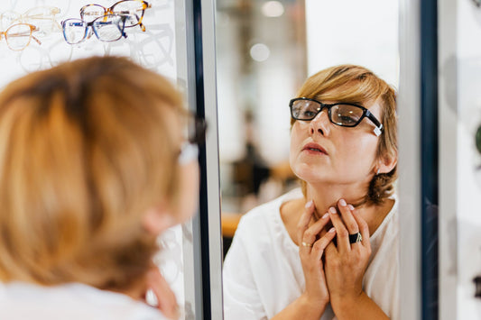 A woman examines her reflection while trying on eyeglasses in an optical store.