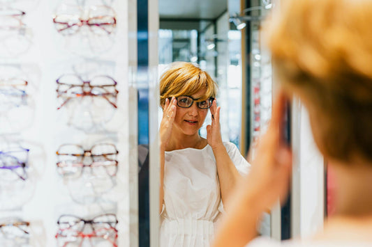 A woman tries on eyeglasses while looking in a mirror at an optician store.