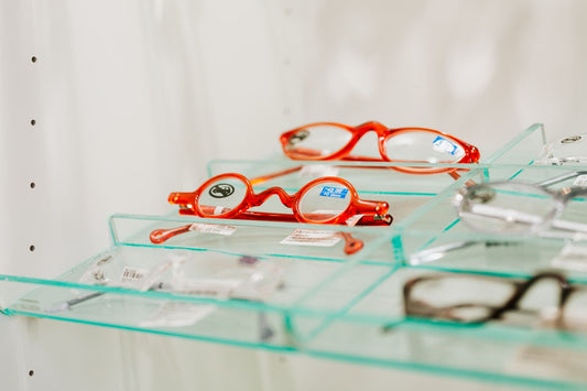 Stylish red eyeglasses displayed on a glass shelf in an eyewear store.