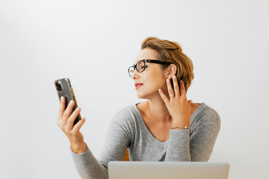 Caucasian woman with eyeglasses and light background taking a selfie indoors.