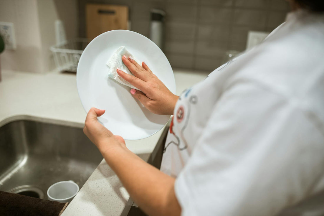 A person cleaning a ceramic plate by hand in a modern kitchen setting.