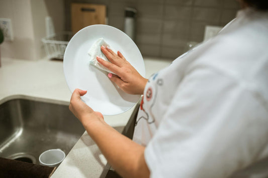 A person cleaning a ceramic plate by hand in a modern kitchen setting.