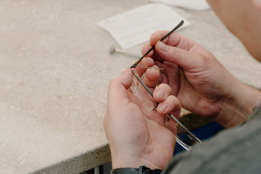 From above of anonymous male master sitting at table and fastening temple with screw while repairing eyeglasses in professional workshop