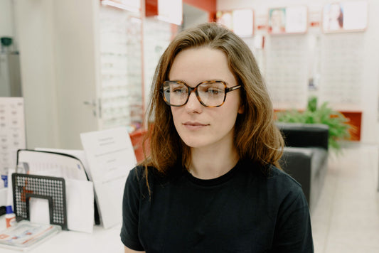 Concentrated female client checking vision while wearing new eyewear while sitting on blurred background in optical clinic