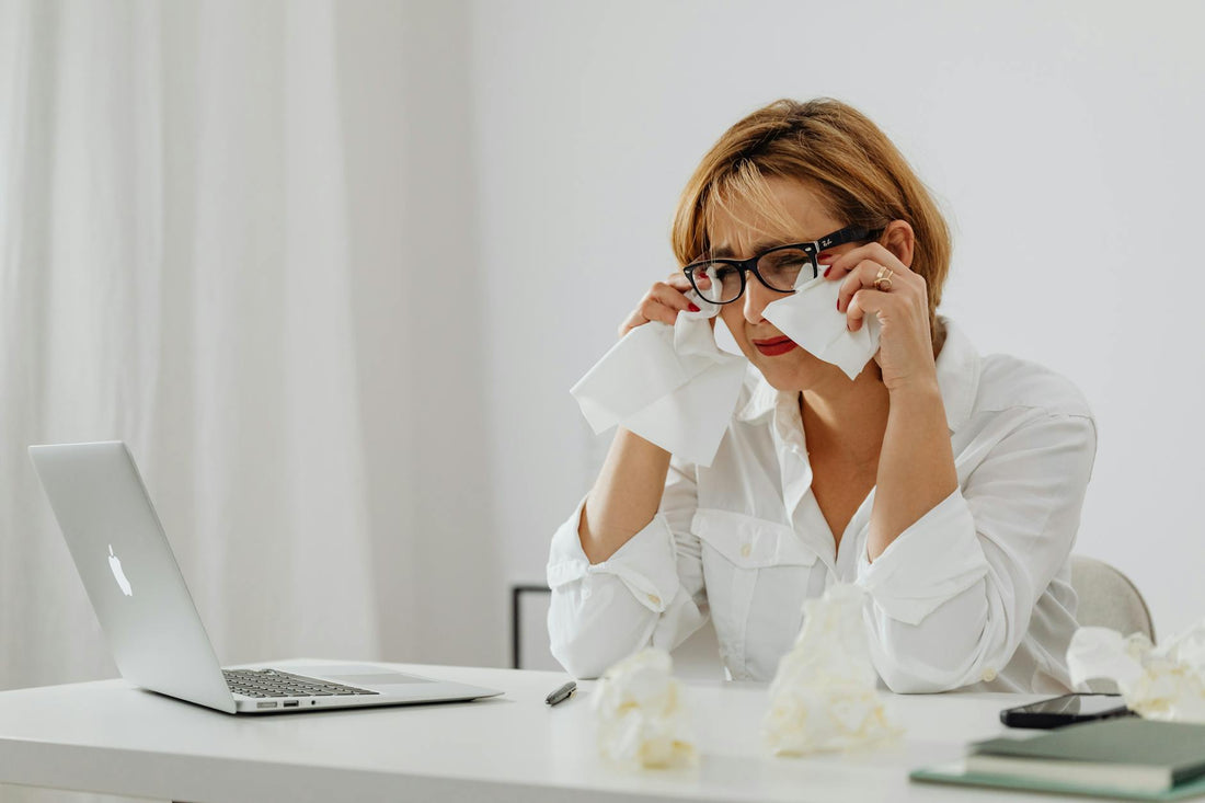 Woman experiencing stress at work using a laptop with tissues on a desk.