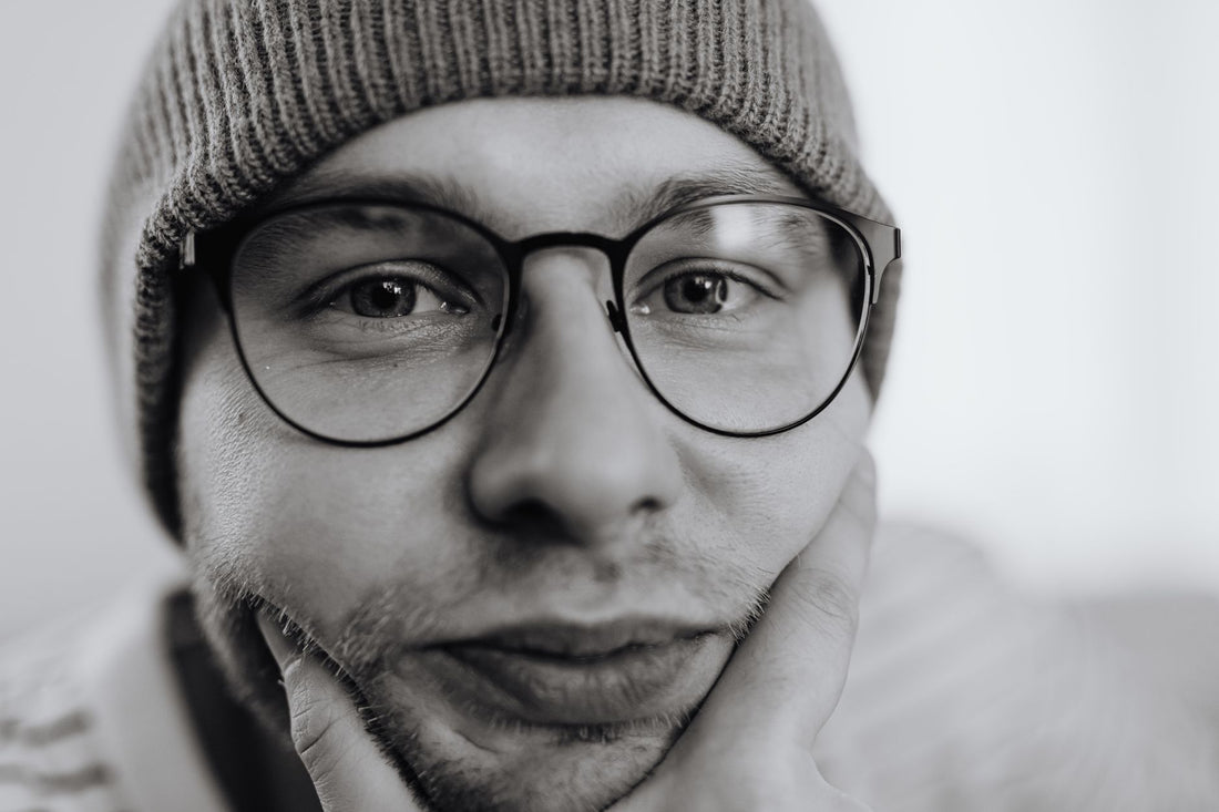 A thoughtful monochrome portrait of a man wearing glasses and a beanie.