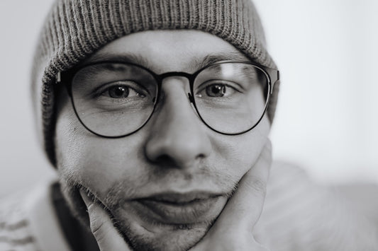 A thoughtful monochrome portrait of a man wearing glasses and a beanie.