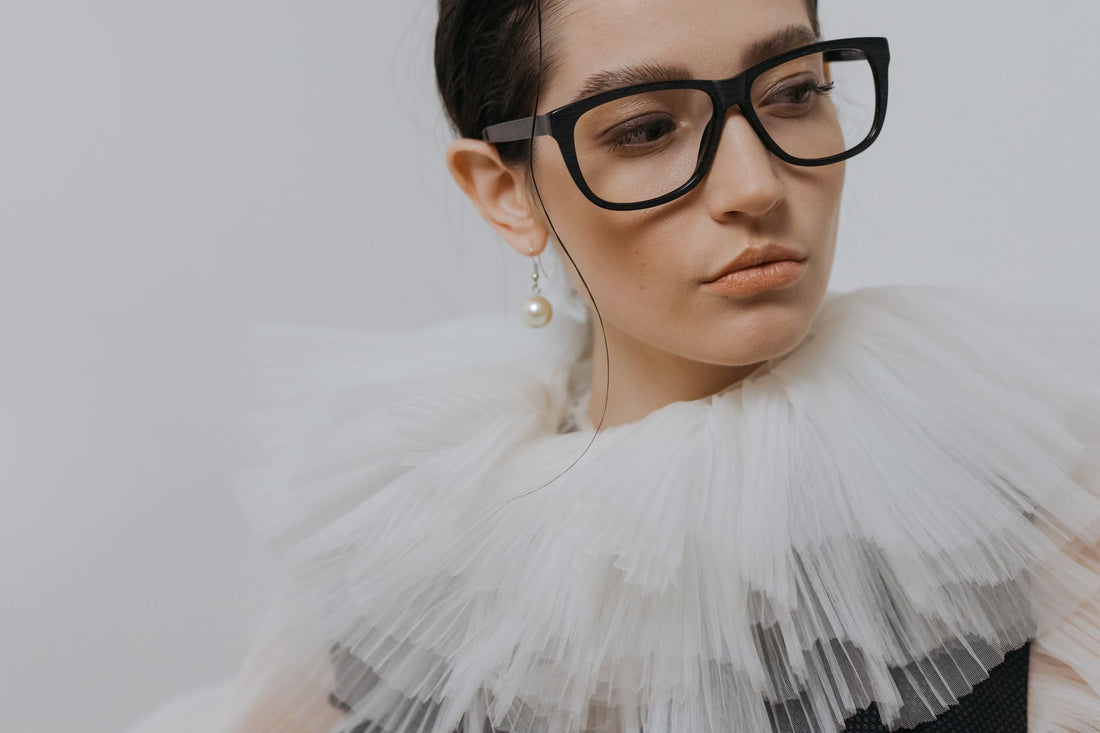 Portrait of a stylish woman in a chiffon collar, wearing glasses and a pearl earring.