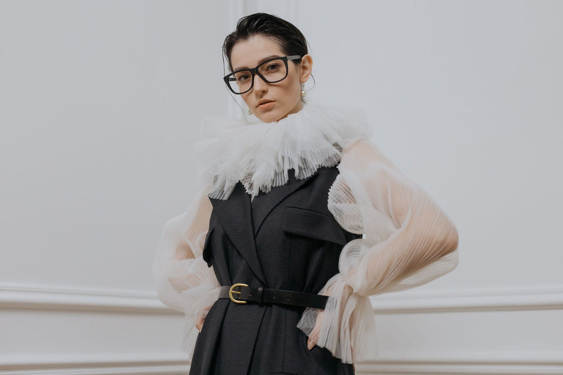 Chic woman in a stylish outfit with eyeglasses posing gracefully indoors.