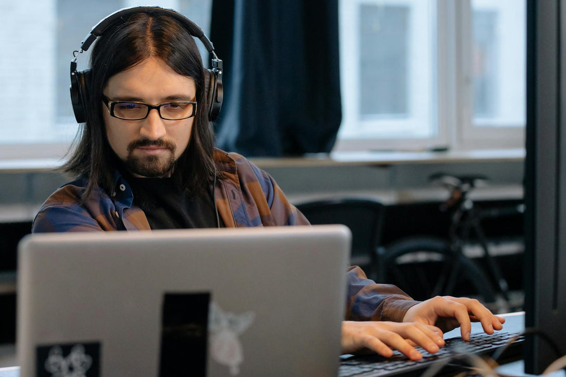 Office worker wearing headphones while concentrating on laptop tasks.